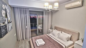 A modern hotel room with a large bed, a nightstand, a wall-mounted air conditioner, and a view of the outdoors through a sliding glass door. - Villa Nefeli (Nea Propontida)