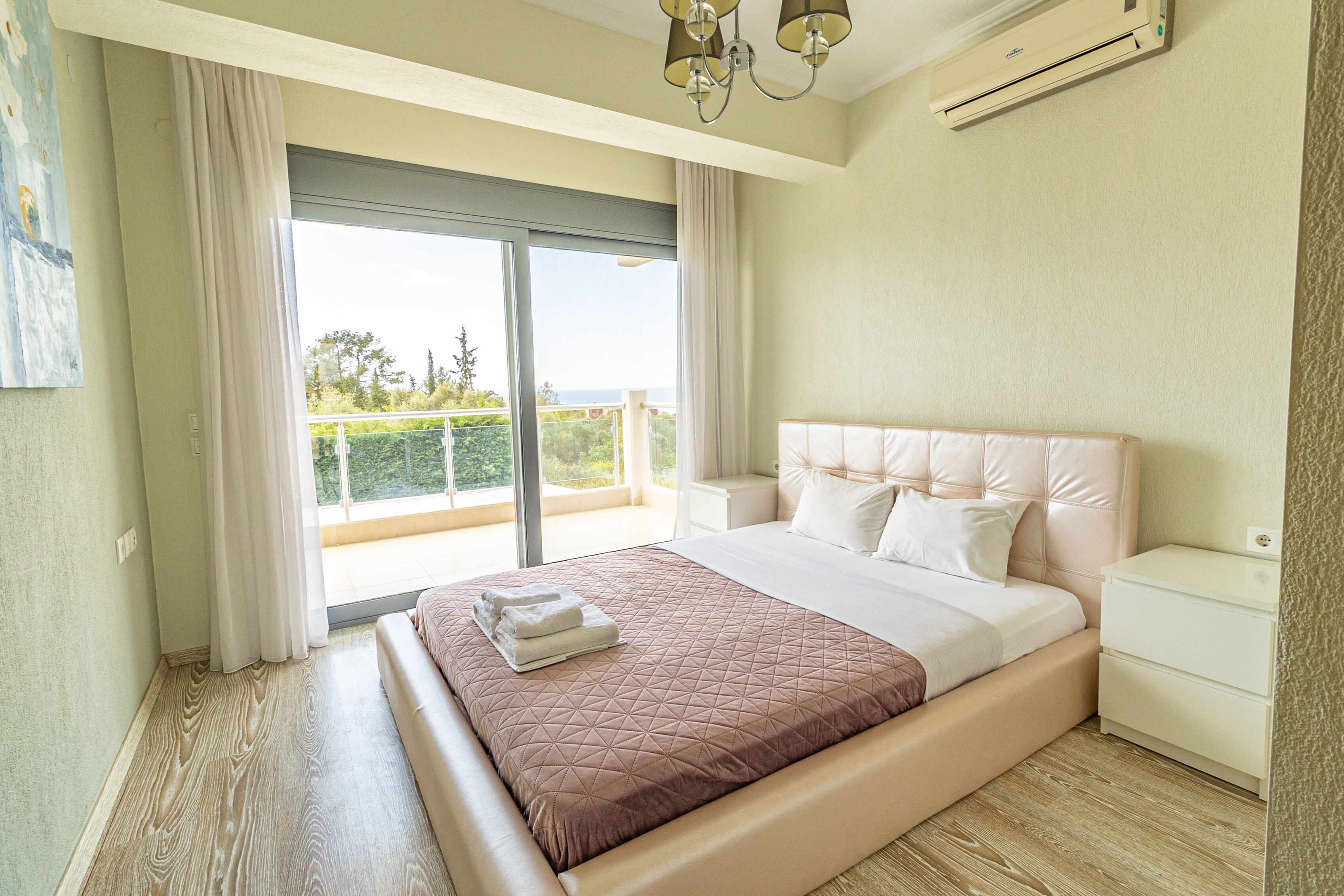 A bedroom with a large bed, a nightstand, a ceiling fan, and a view of the outdoors through a sliding glass door.