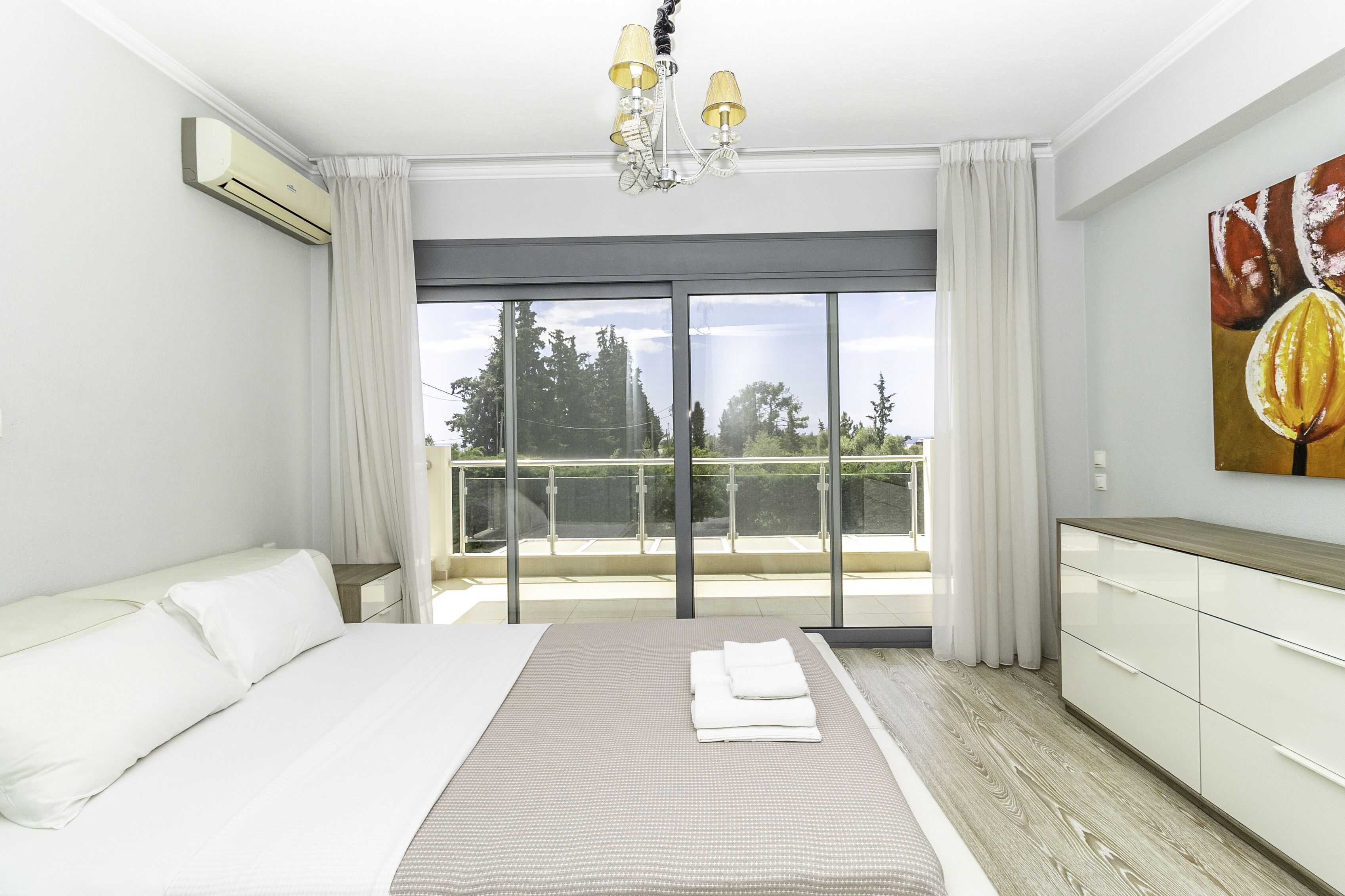 Una habitación de hotel moderna con una cama grande, un balcón con vistas a árboles y un ventilador de techo.