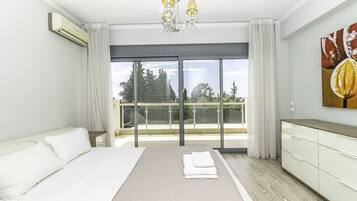 Una habitación de hotel moderna con una cama grande, un balcón con vistas a árboles y un ventilador de techo.