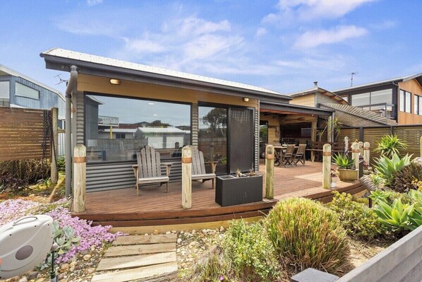 A modern outdoor patio with wooden decking, seating, and potted plants. - Coastal Cottage with Ocean Views (Sunderland Bay)