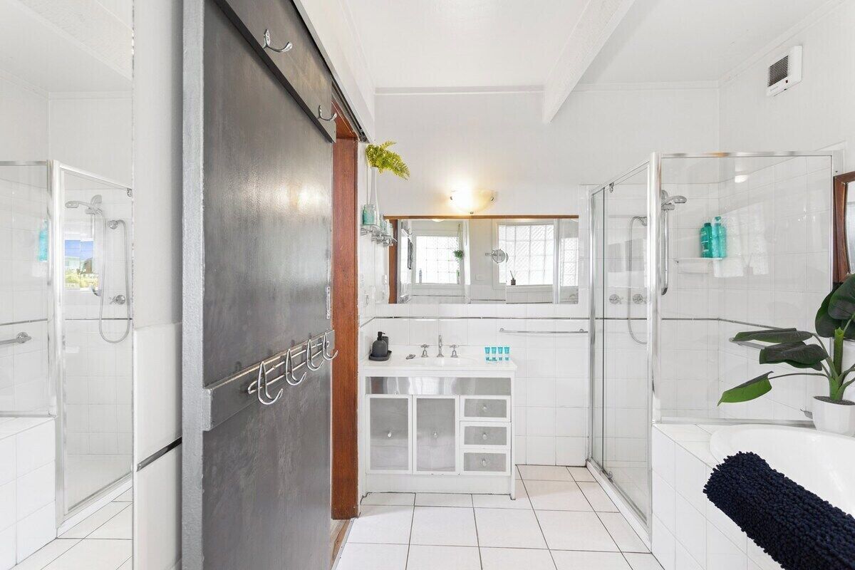 A modern bathroom with a glass shower enclosure, a white vanity with a mirror, and a potted plant.