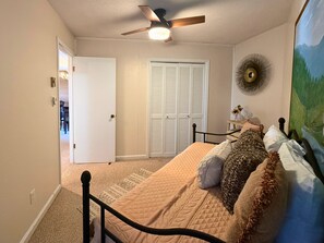 A bedroom with a bed, a ceiling fan, a door, and a wall-mounted fan.