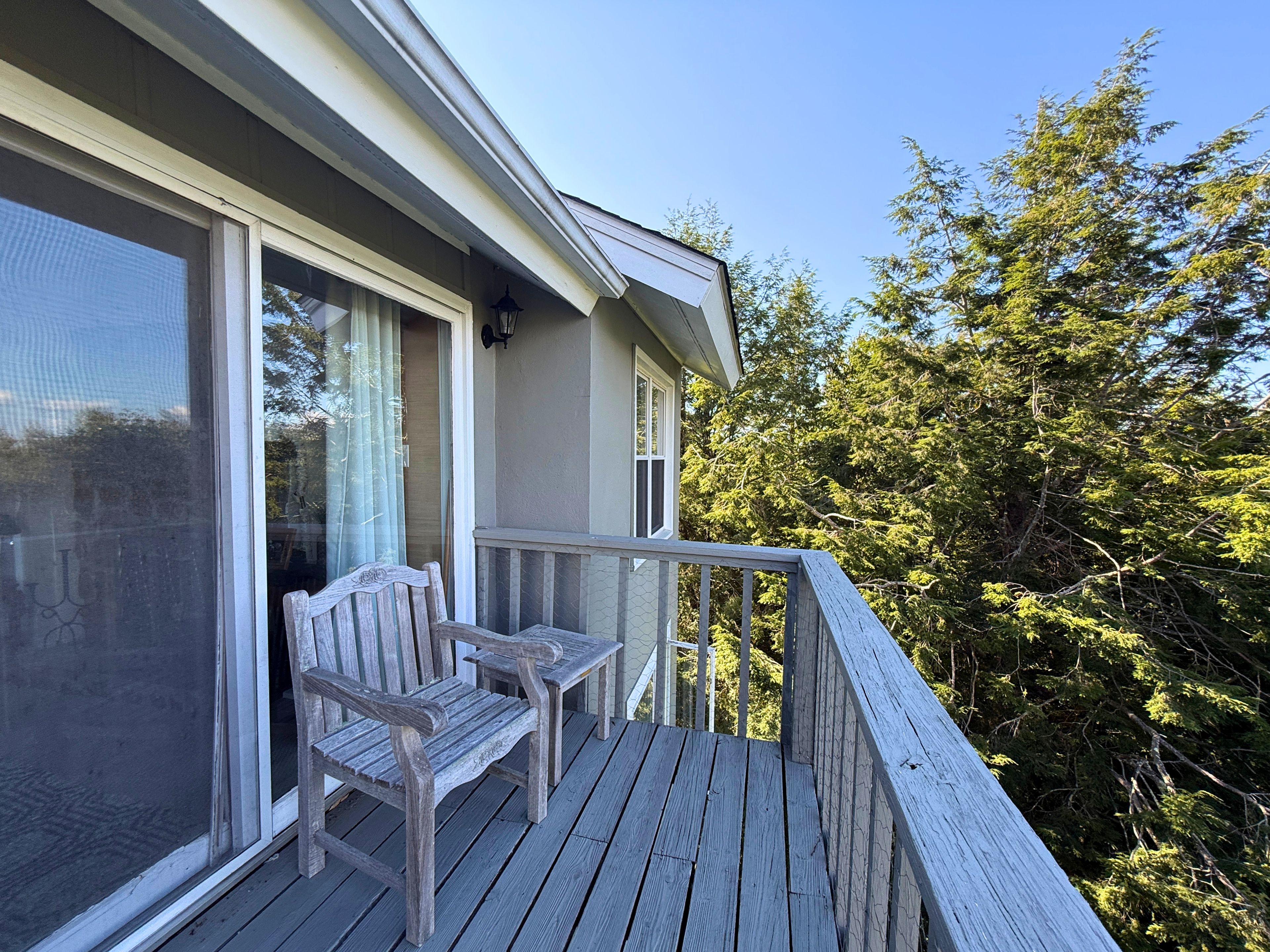 A wooden deck with two chairs and a table, overlooking a forested area.