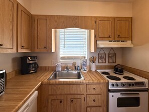 A compact kitchen with wooden cabinets, a stainless steel sink, a stove, and a coffee maker.