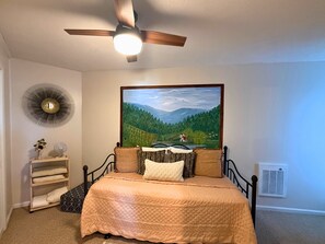A bedroom with a bed, a ceiling fan, a painting, a radiator, and a bedside table with a lamp. - Cozy Mountain Condo with Mountain Views (Sugar Mountain)