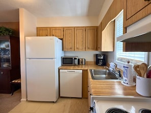 A compact kitchen with wooden cabinets, a white refrigerator, a microwave, a coffee maker, and a sink with utensils. - Cozy Mountain Condo with Mountain Views (Sugar Mountain)