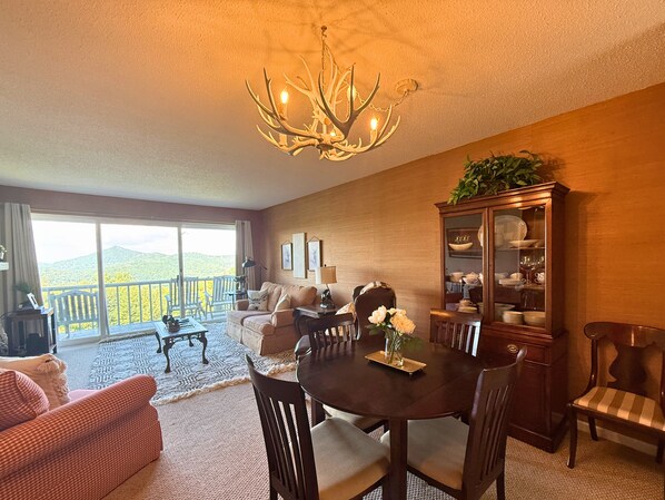 A dining area with a chandelier, a dining table, chairs, a cabinet with dishes, and a view of a balcony with a railing.