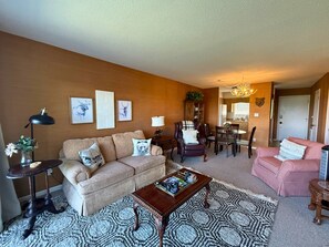 A living room with a sofa, armchairs, a coffee table, and a dining area with chairs and a table.