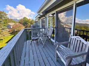 A wooden deck with chairs and a table, overlooking a landscaped garden and distant mountains.