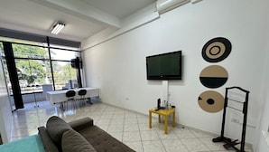 A modern living room with a sofa, a TV, and a small table with electronic devices. - Loft São João Exclusive (Sao Joao da Boa Vista)
