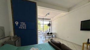 A hotel room with a bed, a desk, a chair, a TV, and a view of the outdoors. - Loft São João Exclusive (Sao Joao da Boa Vista)