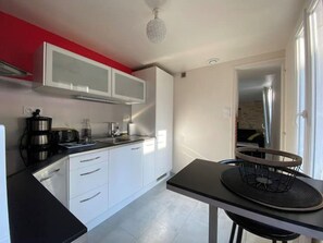 Une cuisine compacte avec des meubles blancs, un plan de travail noir et un petit coin repas comprenant une table et une chaise noires.