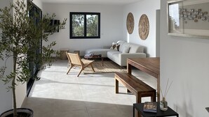 Un área de estar amplia con sofá, mesa de centro y sillas. Hay un ventanal grande que proporciona luz natural y vistas al exterior.