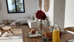 Un comedor con una mesa de madera preparada para el desayuno, con bollos y una botella de zumo de naranja.