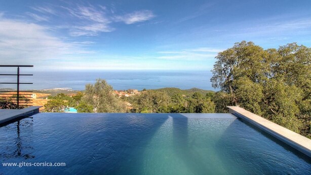 Una piscina infinita con una vista despejada del océano y colinas al fondo.
