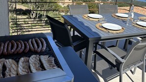 Un patio con una parrilla, mobiliario exterior y una vista panorámica de la costa.