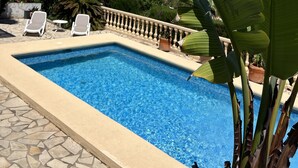 Une piscine avec vue sur la mer, entourée de chaises longues et de plantes en pot.