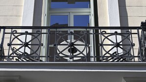Ein Balkon mit aufwendiger schmiedeeiserner Geländer und einem Fenster mit weißem Rahmen.