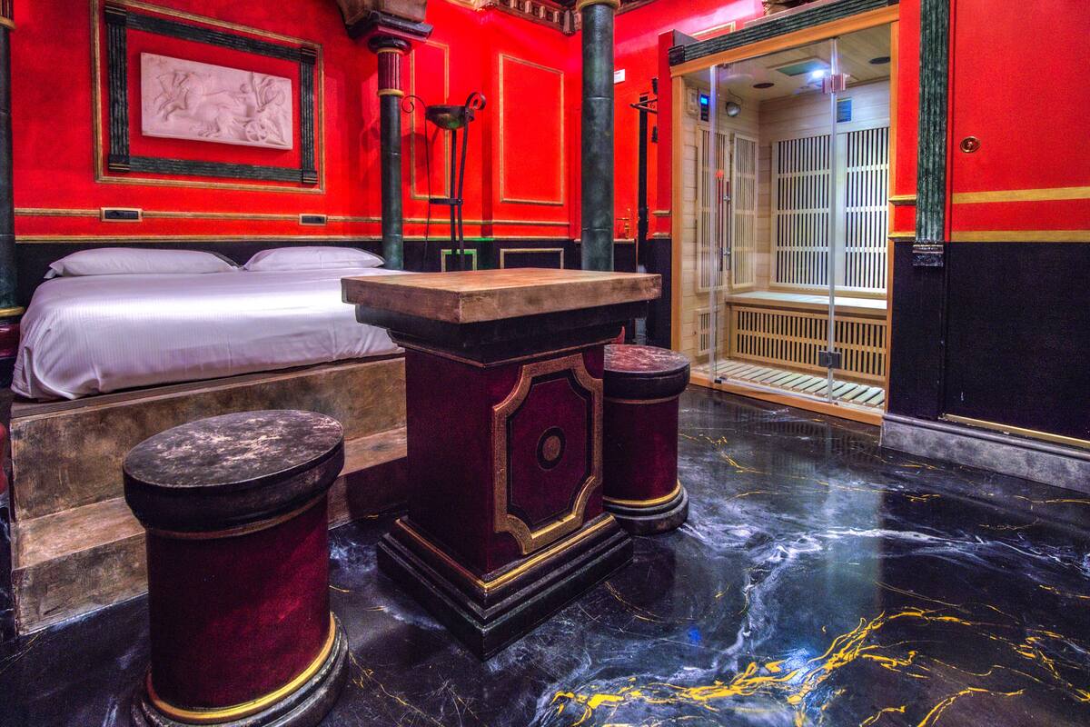 A room with a bed, a marble floor, and a red wall with a framed artwork.