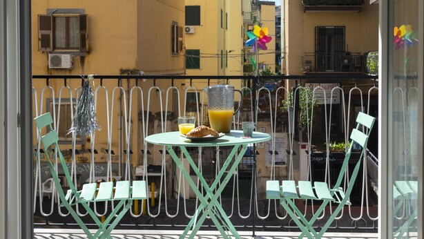 A balcony with a table and chairs, a glass of orange juice, and a croissant. - MarGab B&B Green Room (Napoli)