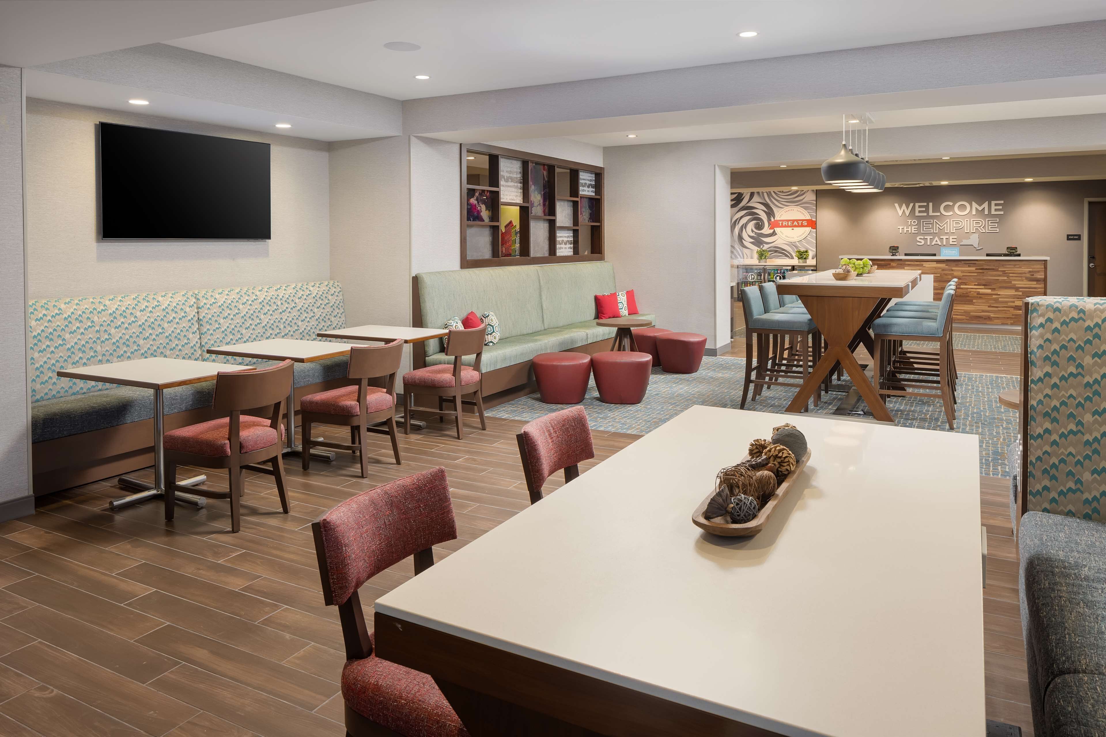 Un hall d’hôtel moderne doté d’un comptoir d’accueil, de coins salon et d’un grand téléviseur à écran plat fixé au mur.