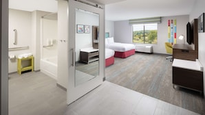 Ein modernes Hotelzimmer mit einer Schiebetür zum Badezimmer, einem Bett mit rotem Akzent, einem Schreibtisch und Blick ins Freie.