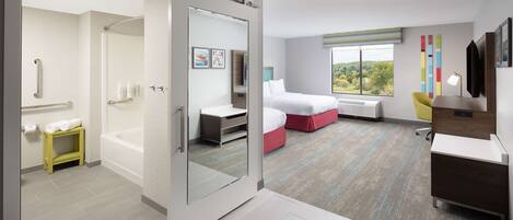 Habitación de hotel moderna con puerta corredera que da al baño, cama con detalles en rojo, escritorio y vista al exterior.