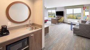 Ein modernes Hotelzimmer mit Küchenbereich, einer Sitzecke mit Sofa und Schreibtisch, einem Flachbildfernseher und einem großen Fenster mit schöner Aussicht.
