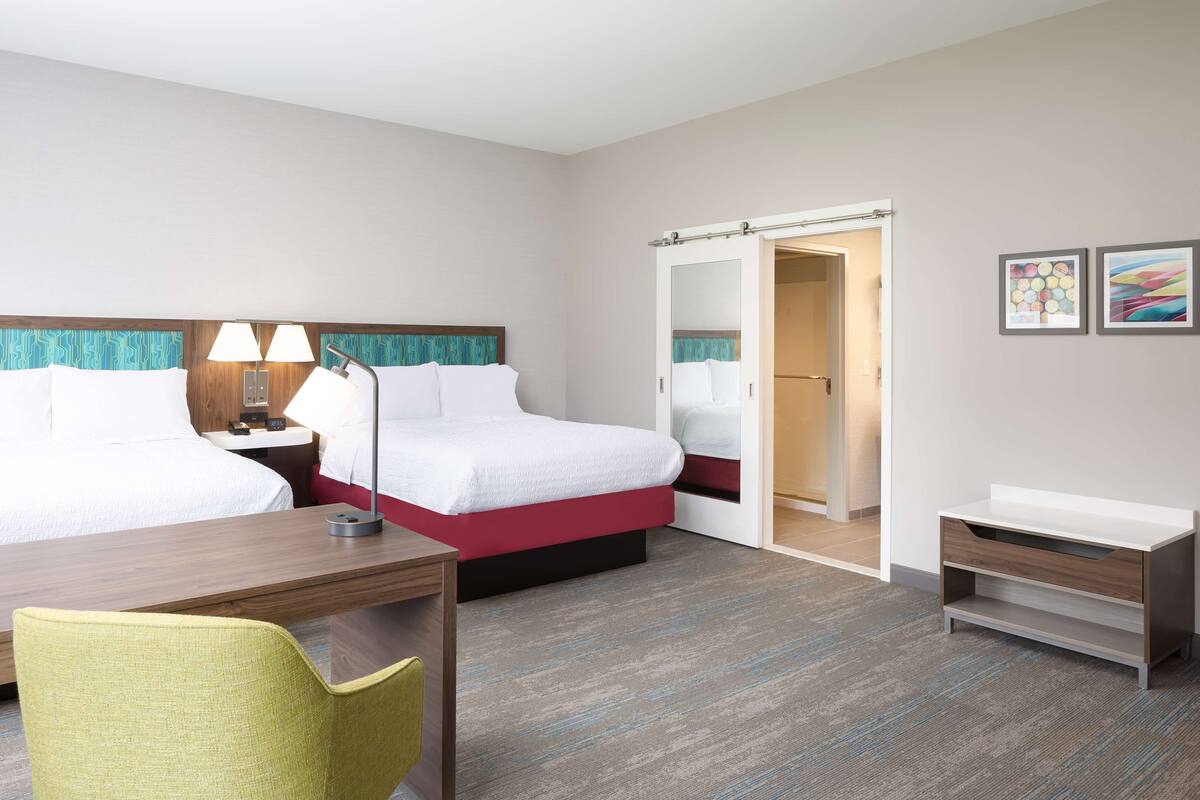 Hotellihuone, jossa on kaksi sänkyä, työpöytä, tuoli, yöpöytä valaisimilla, vaatekaappi ja pieni yöpöytä.
