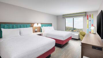 Quarto de hotel com duas camas, uma escrivaninha, uma cadeira e uma televisão.