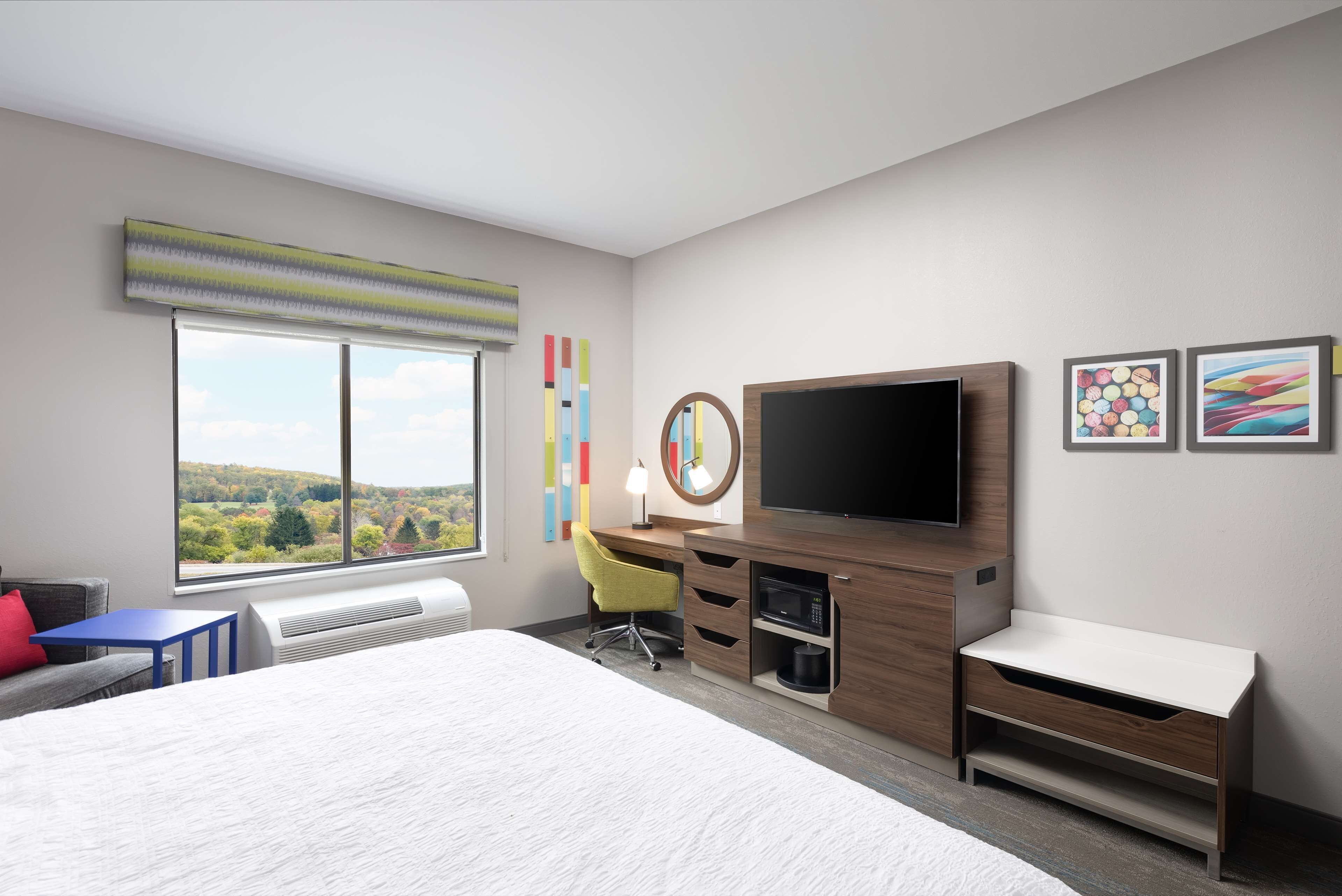 Una habitación de hotel moderna con una cama grande, un escritorio con una silla, un televisor de pantalla plana y una ventana con vistas al exterior.