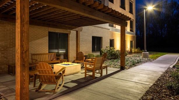 Eine Terrassenanlage im Freien mit Holzmöbeln und einem Feuerkorb, angrenzend an ein Gebäude mit Ziegelwänden und großen Fenstern.