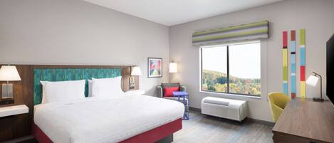 A hotel room with a large bed, a desk, a chair, a window with a view, and a wall with colorful decor.