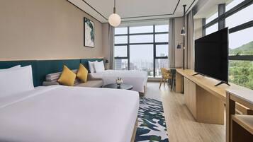 A hotel room with two beds, a desk, a TV, and a large window with a city view.