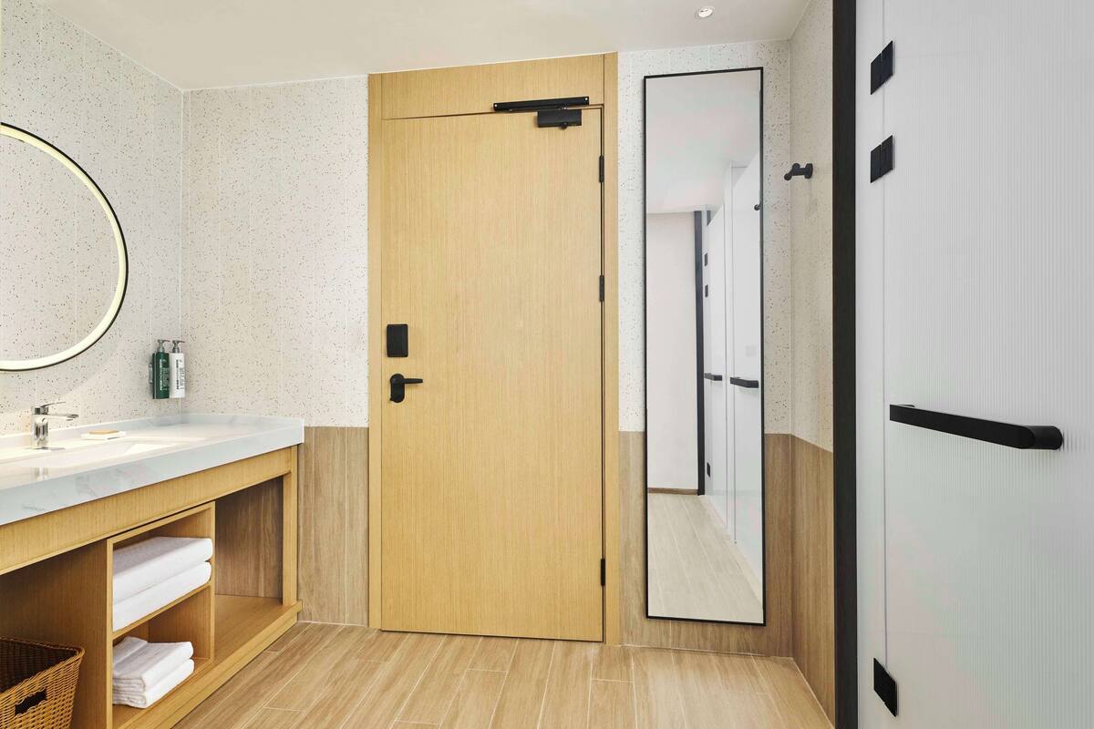 A modern bathroom with a wooden door, a large mirror, and a white sink.