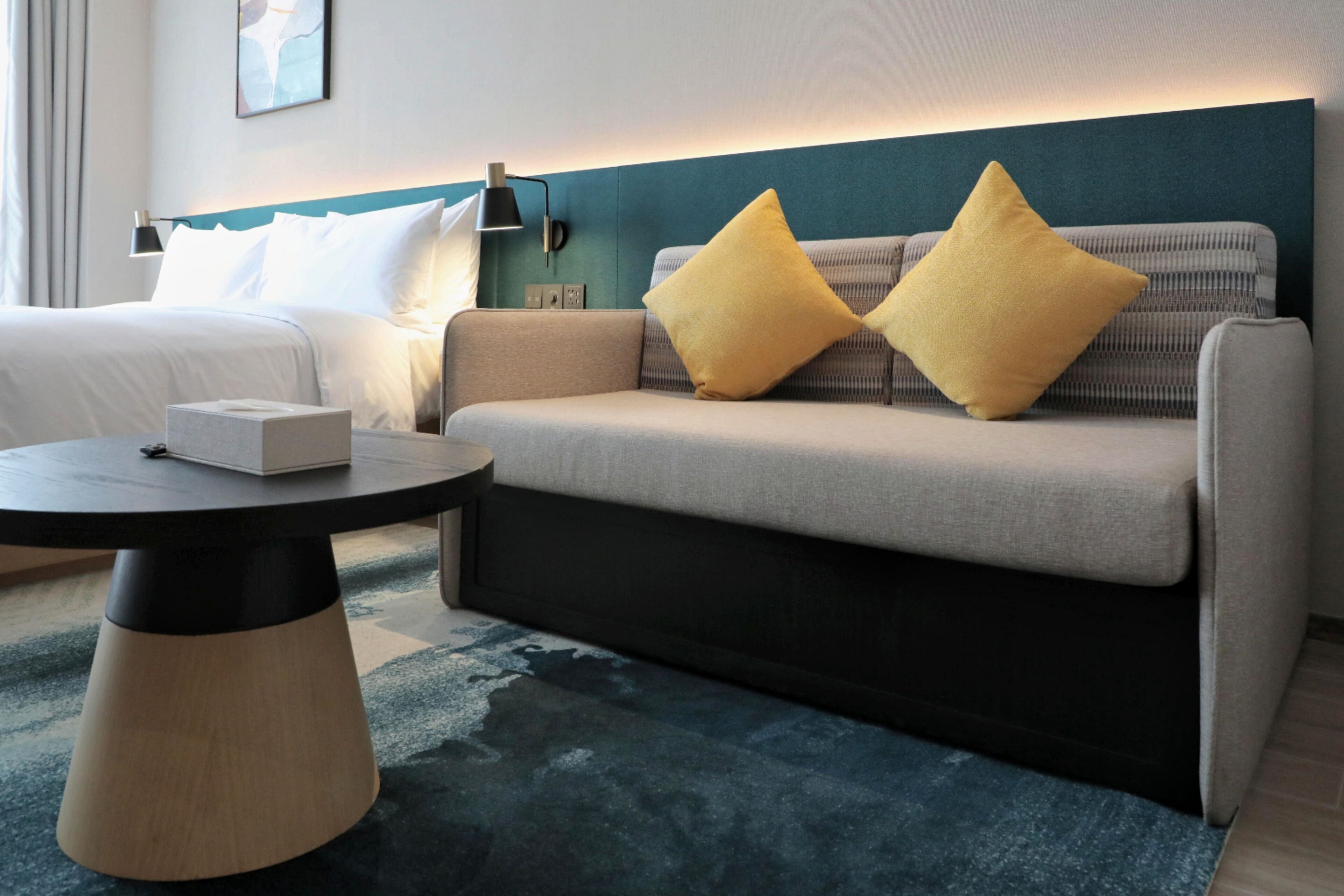 Una habitación de hotel moderna con un sofá, una mesa redonda de centro y una lámpara de pared.