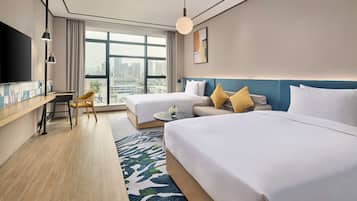 A hotel room with two beds, a desk, a chair, a TV, and a large window with a city view.