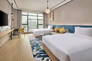 Habitación de hotel con dos camas, un escritorio, una silla, un televisor y un ventanal con vistas a la ciudad.