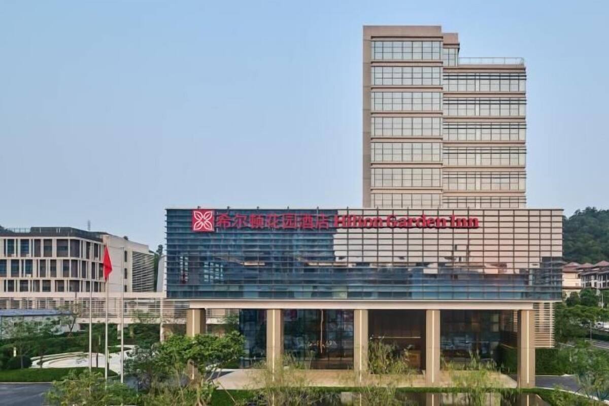 A modern hotel with a prominent sign, a tall adjacent building, and a landscaped area in front.
