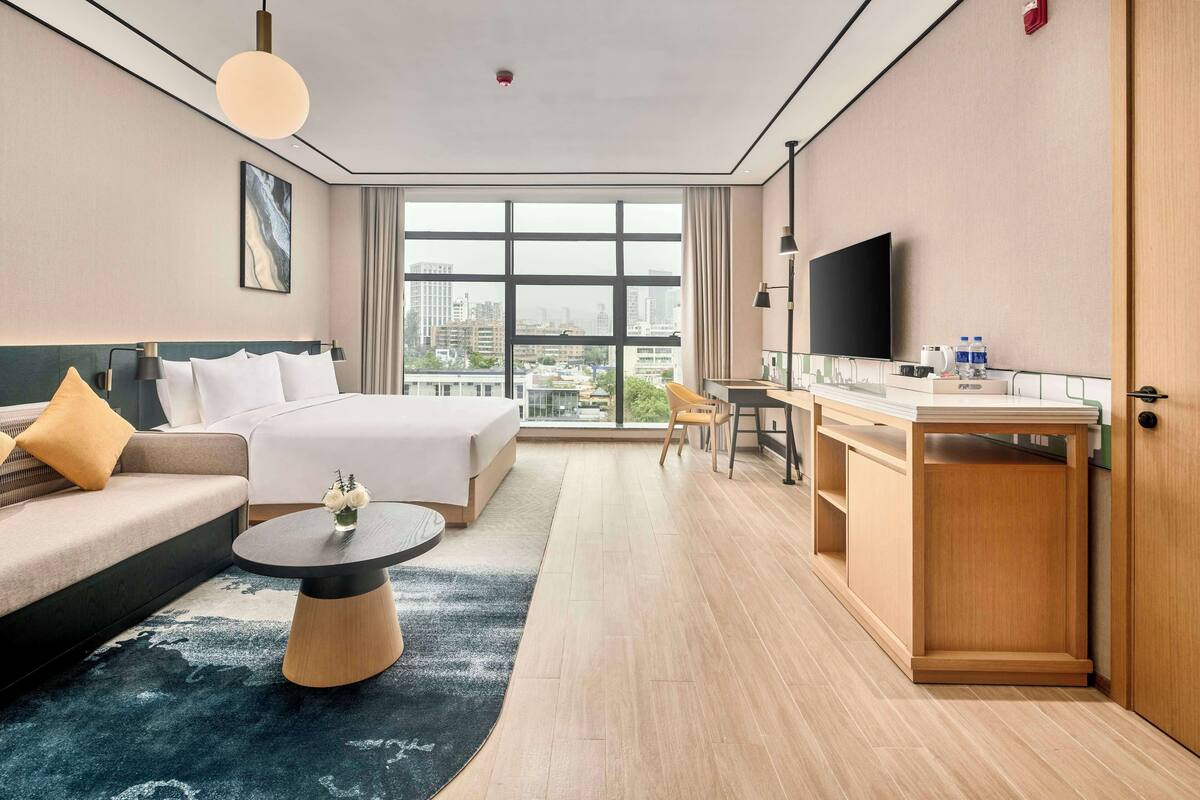 A modern hotel room with a large bed, a sofa, a desk, and a TV.