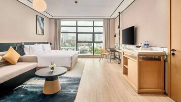 A modern hotel room with a large bed, a sofa, a desk, and a TV.