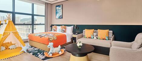 A modern hotel room with a large bed, a sofa, a coffee table, and a play area including a tent and toys.