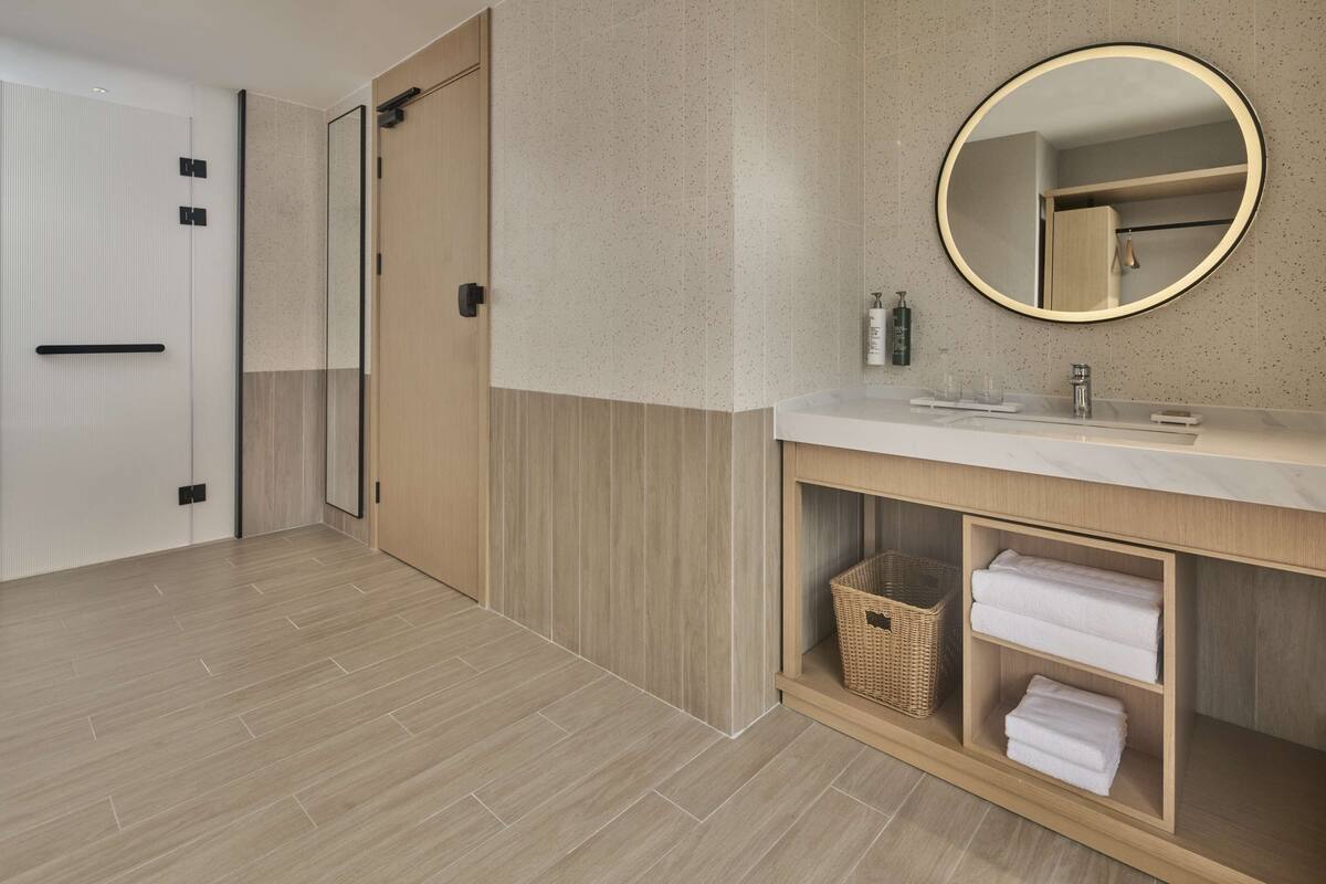 A modern bathroom with a wooden vanity, a round mirror, and a towel rack.