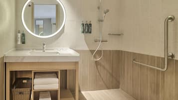 Uma casa de banho moderna com lavatório, espelho, chuveiro e barras de apoio.