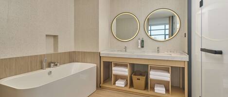 A modern bathroom with a freestanding bathtub, two round mirrors, and a wooden vanity with built-in shelves.