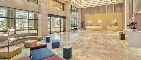 A spacious lobby with a reception desk, seating areas, and large windows offering views of the outdoors.