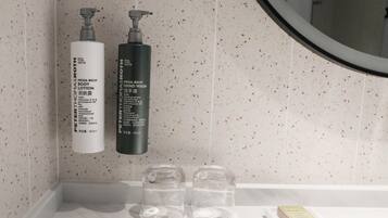 A bathroom with two bottles of Mega-Rich body lotion and hand wash, two clear glasses, and a small book on the counter.