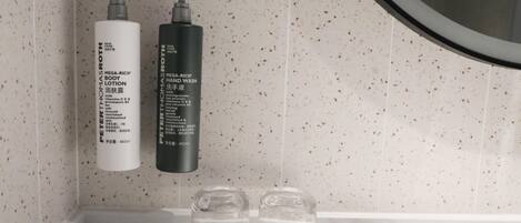 A bathroom with two bottles of Mega-Rich body lotion and hand wash, two clear glasses, and a small book on the counter.