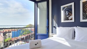 Une chambre d’hôtel avec un lit, une serviette blanche et une vue sur le paysage urbain, visible à travers une porte ouverte.